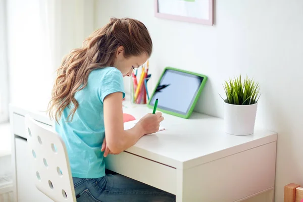 家里有平板电脑的女孩在笔记本上写字 — 图库照片