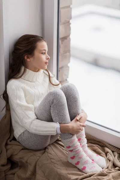 Verdrietig meisje zit op dorpel thuis venster in de winter — Stockfoto