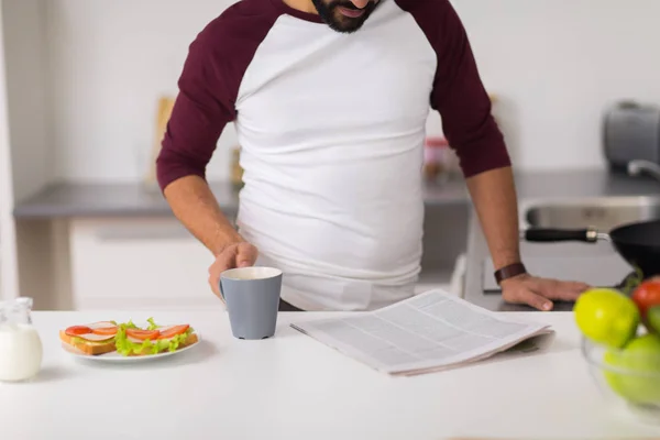 Gazete okuma ve evde mutfak yemek adam — Stok fotoğraf