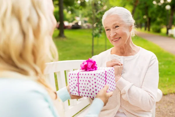 Daughter giving present to senior mother at park — Stock Photo, Image