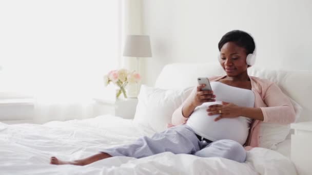 Беременная женщина в наушниках со смартфоном — стоковое видео