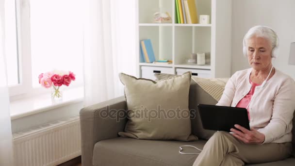 Senior vrouw met tablet pc en hoofdtelefoon thuis — Stockvideo