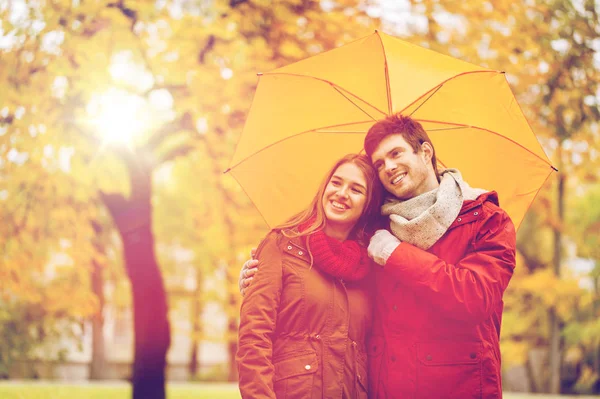 Coppia sorridente con ombrellone nel parco autunnale — Foto Stock