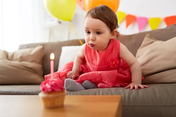 Flicka som blåser till ljus på födelsedag cupcake hemma Stockbild