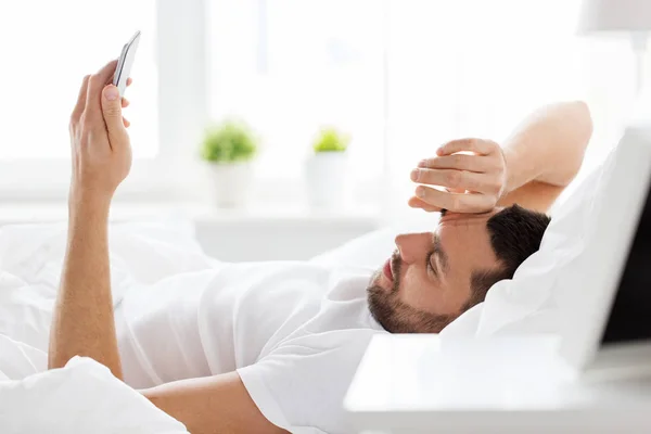 Joven con teléfono inteligente en la cama por la mañana — Foto de Stock