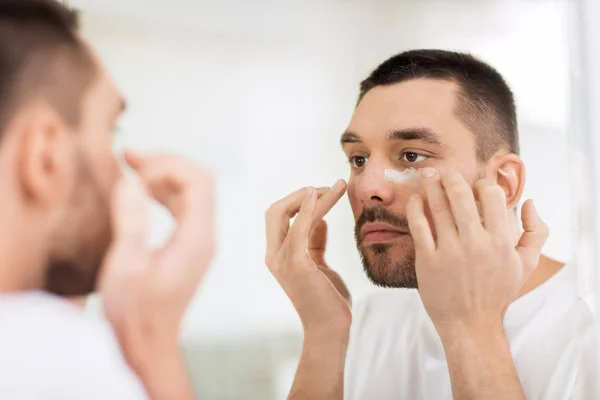 Young man applying cream to face at bathroom — Stock Photo, Image