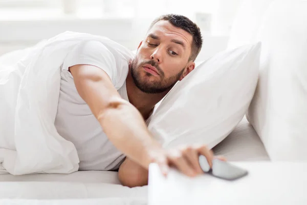 Jovem chegando para smartphone na cama — Fotografia de Stock