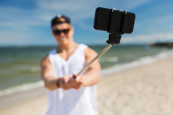 Мужчина со смартфоном делает селфи на летнем пляже — стоковое фото