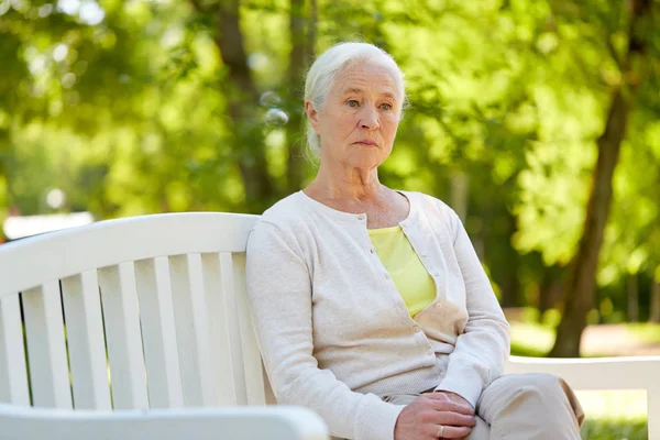 Smutné, starší žena sedící na lavičce v parku léta — Stock fotografie