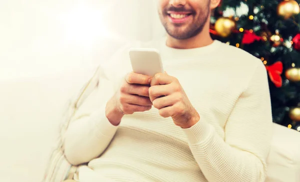 Lächelnder Mann mit Smartphone zu Weihnachten zu Hause — Stockfoto