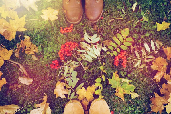 Pés em botas com amoras e folhas de outono — Fotografia de Stock