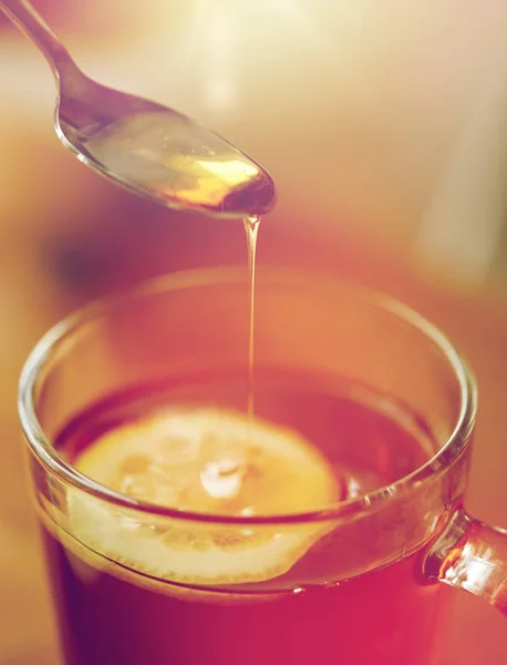 Primo piano di donna che aggiunge miele al tè con limone — Foto Stock