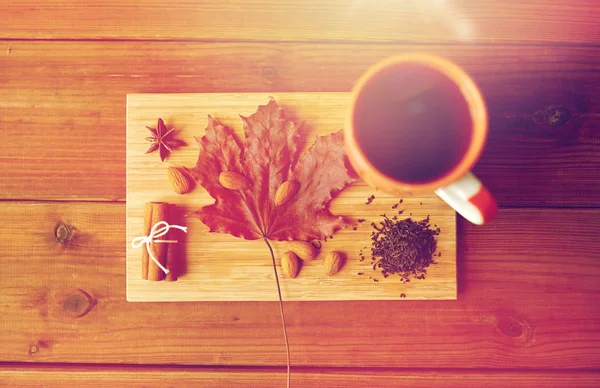 Xícara de chá, folha de bordo e amêndoa em tábua de madeira — Fotografia de Stock