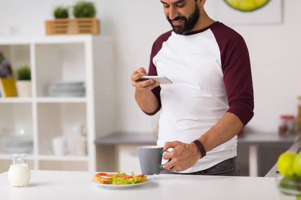 Hombre con smartphone y café comiendo en casa —  Fotos de Stock