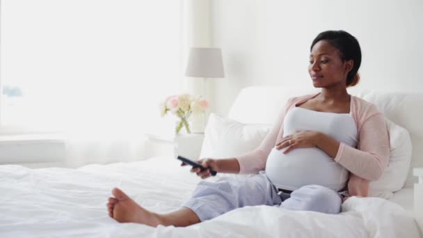 Mujer africana embarazada viendo la televisión en la cama en casa — Vídeos de Stock