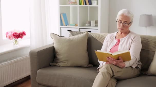 Senior vrouw in glazen lezen boek thuis — Stockvideo