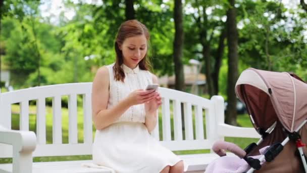 Madre feliz con smartphone y cochecito en el parque — Vídeo de stock