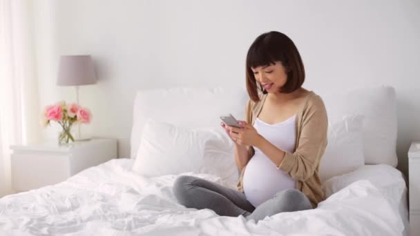 Glad gravid asiatisk kvinna med smartphone i sängen — Stockvideo