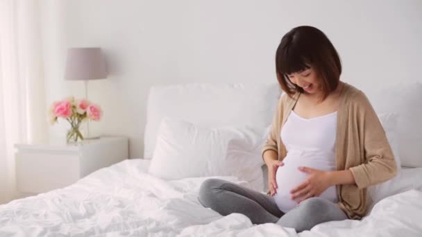 Boldog terhes ázsiai nő ül ágyas otthon — Stock videók