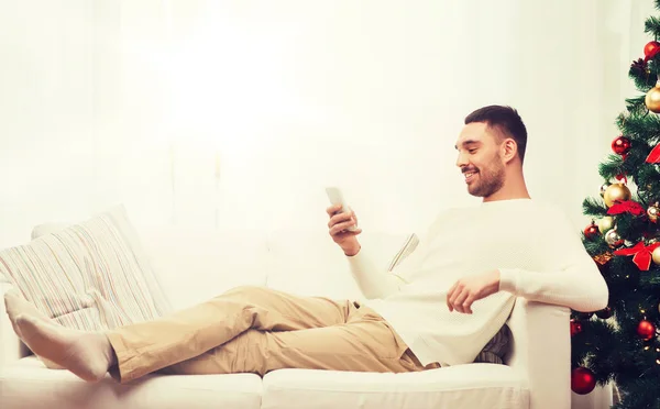 Lächelnder Mann mit Smartphone zu Weihnachten zu Hause — Stockfoto