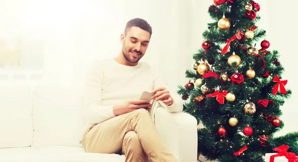 Lächelnder Mann mit Smartphone zu Weihnachten zu Hause — Stockfoto