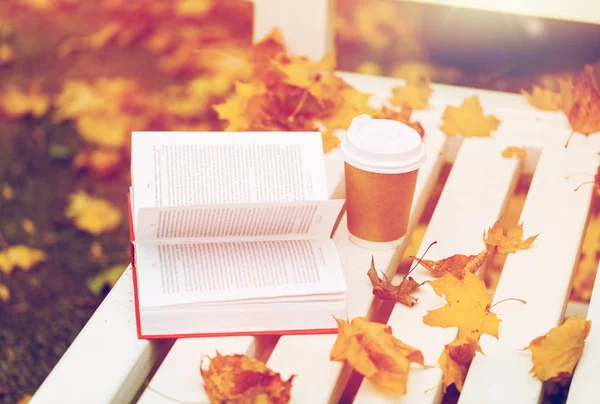 Libro abierto y taza de café en el banco en el parque de otoño — Foto de Stock