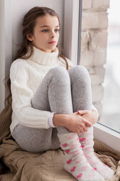Menina triste sentado no peitoril em casa janela no inverno — Fotografia de Stock