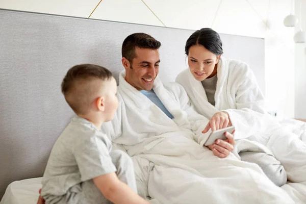 Famiglia felice con smartphone a letto in camera d'albergo — Foto Stock