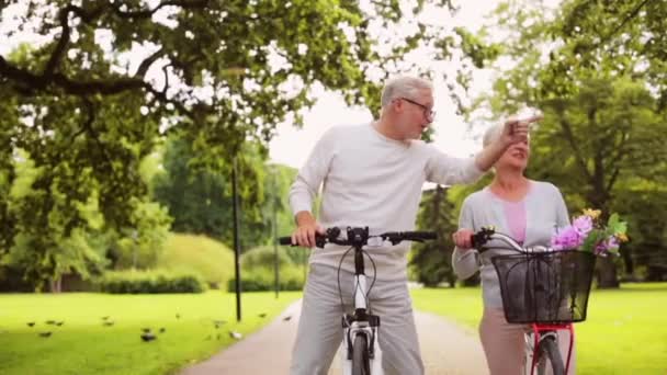 Feliz pareja mayor montando bicicletas en el parque de verano — Vídeos de Stock