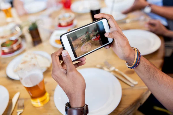 Mains avec smartphone picturant la nourriture au restaurant — Photo