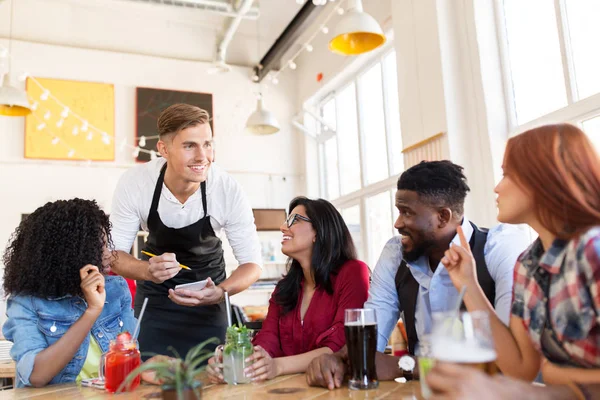 Waiter and friends with menu and drinks at bar — Stock Photo, Image