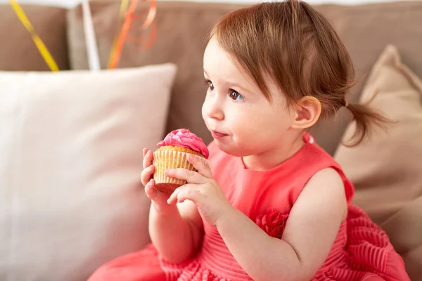 Happy baby flicka äter cupcake på födelsedagsfest — Stockfoto