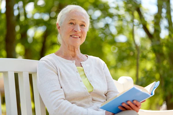 Счастливая пожилая женщина читает книгу в летнем парке — стоковое фото