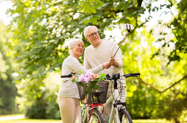 Пожилая пара с велосипедами делает селфи в парке — стоковое фото