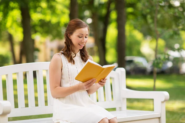 Χαμογελαστή νεαρή γυναίκα διαβάζει βιβλίο στο πάρκο το καλοκαίρι — Φωτογραφία Αρχείου