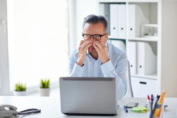 Уставший бизнесмен в очках с ноутбуком в офисе — стоковое фото
