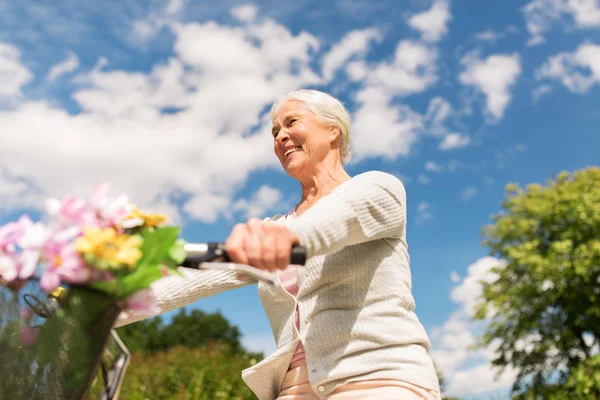 Счастливая пожилая женщина на велосипеде в летнем парке — стоковое фото