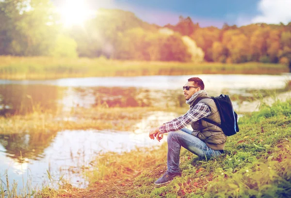 Hombre con mochila descansando en la orilla del río — Foto de Stock