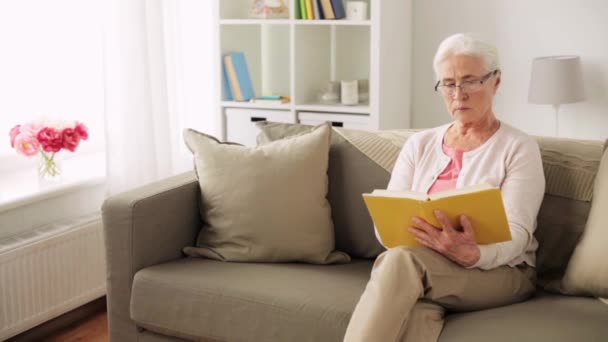 Seniorin mit Brille liest Buch zu Hause — Stockvideo