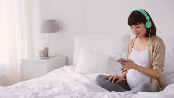 Pregnant asian woman in headphones with smartphone — Stock Video