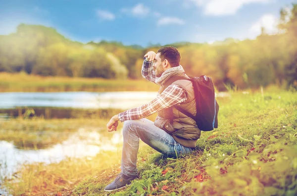 Smiling man with backpack resting on river bank — Stock Photo, Image