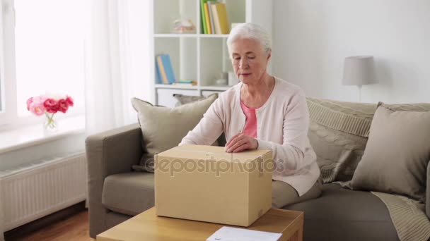 Старшая женщина открывает коробку для посылок дома — стоковое видео