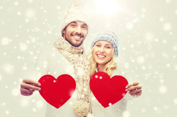 Casal sorridente em roupas de inverno com corações vermelhos — Fotografia de Stock