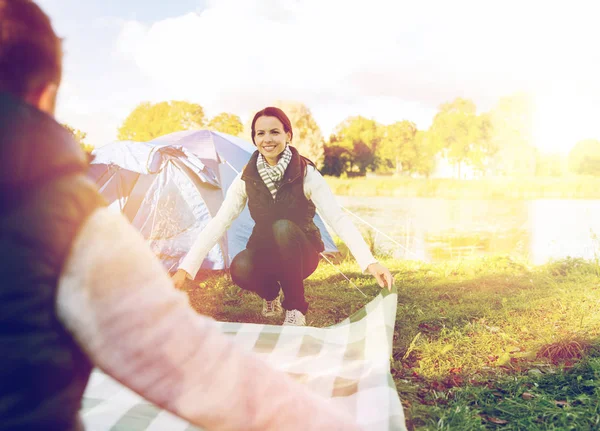 Happy couple with picnic blanket at campsite — Stock Photo, Image
