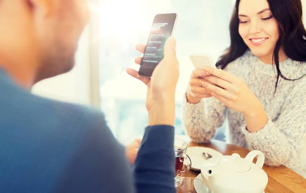 Feliz pareja con teléfonos inteligentes beber té en la cafetería —  Fotos de Stock