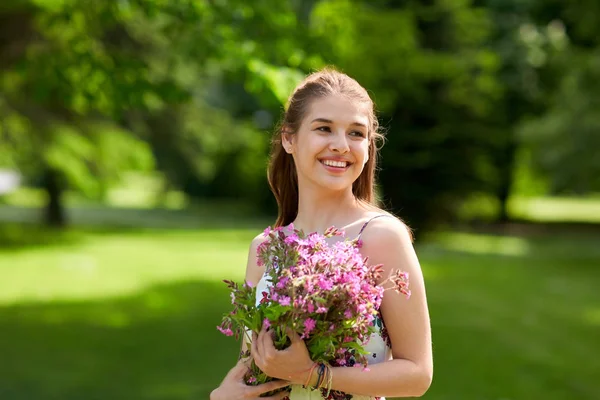 Szczęśliwa młoda kobieta z kwiatami w lato park — Zdjęcie stockowe