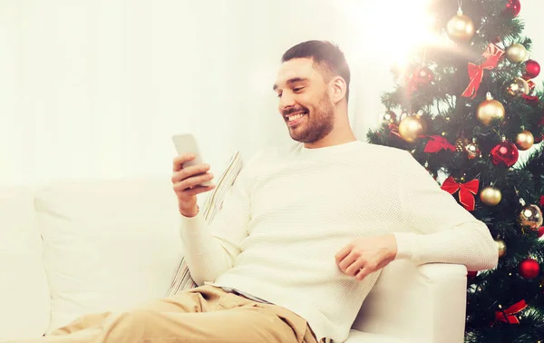 スマート フォンで自宅のクリスマスの笑みを浮かべて男 — ストック写真