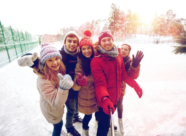 Happy friends with smartphone on ice skating rink — Stock Photo, Image
