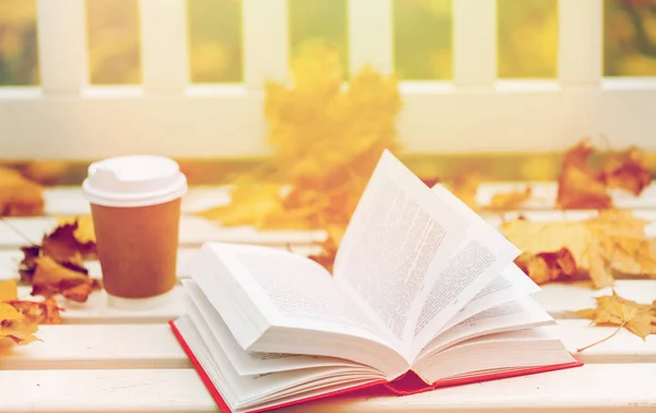 Открытая книга и чашка кофе на скамейке в осеннем парке — стоковое фото