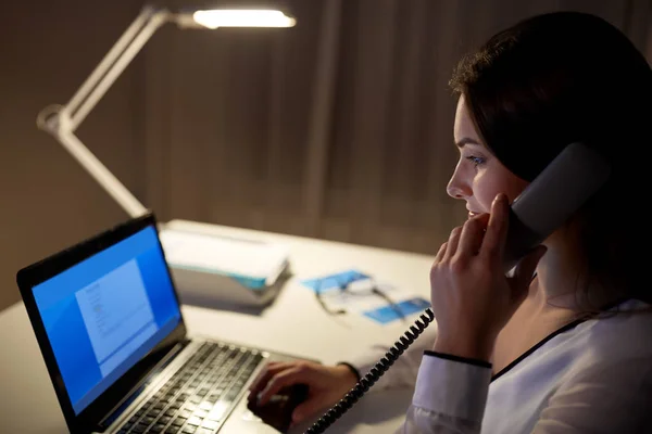 Woman with laptop calling on phone at night office — Stock Photo, Image